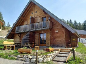 A wooden cabin with a balcony, a staircase, and a stone foundation. - Cozy Chalet, Sleeps 7, Pool & Sauna Access, Near Shops & Restaurants (Le Dévoluy-Agnières-en-Dévoluy)