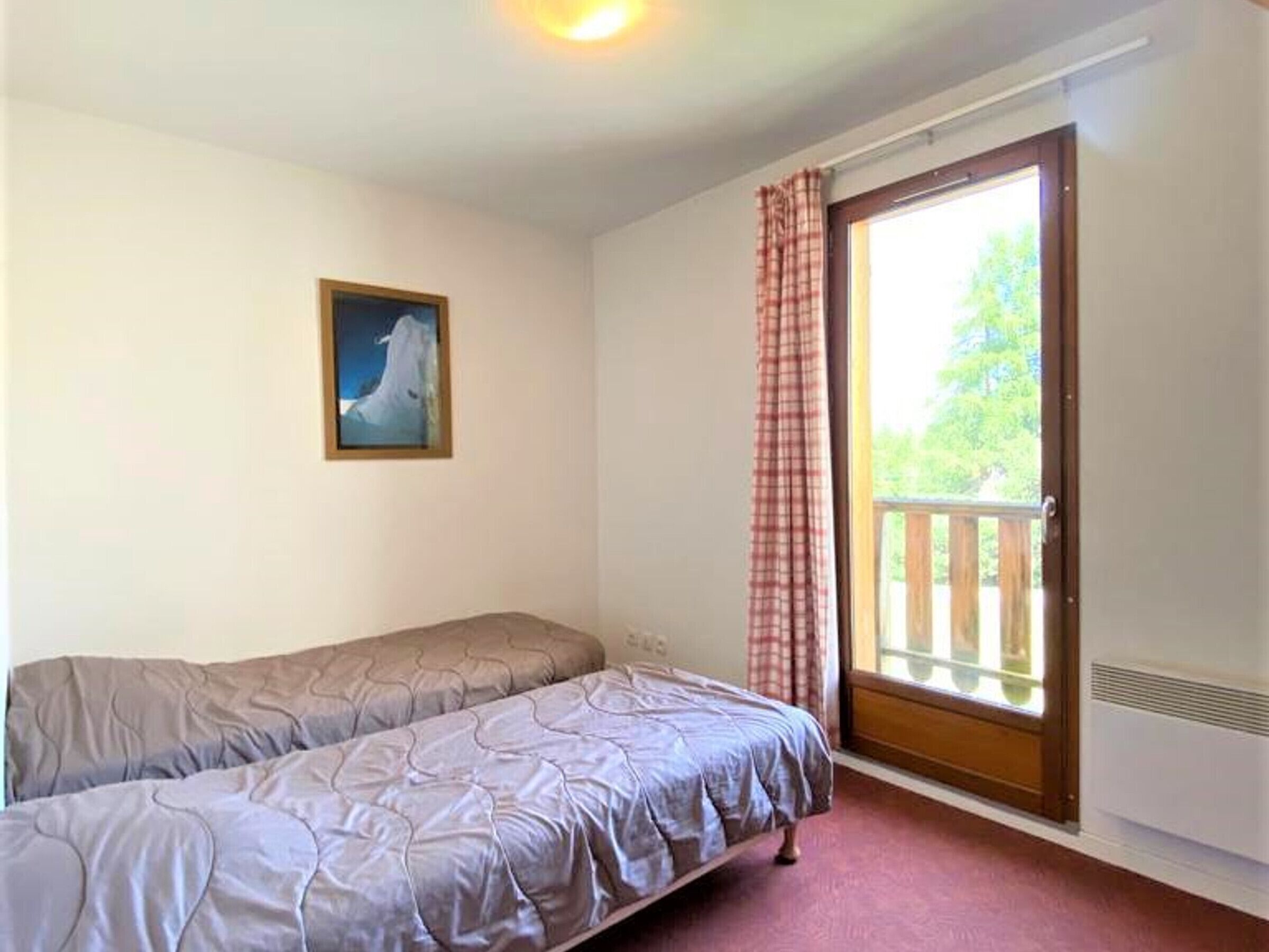 Un dormitorio con una cama individual, un ventanal con vista a follaje y un cuadro en la pared.