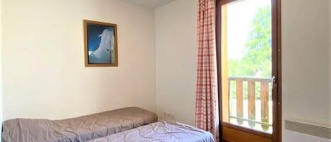 Un dormitorio con una cama individual, un ventanal con vista a follaje y un cuadro en la pared.