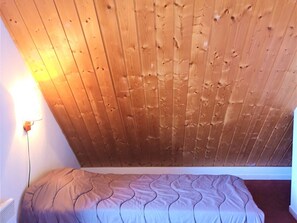 Une petite chambre avec un lit simple, un plafond en pente et un luminaire fixé au mur.