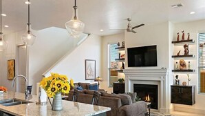 A modern living room with a fireplace, a TV mounted above it, and a dining area with a kitchen island.