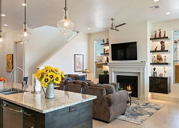 Una sala de estar moderna con chimenea, un televisor montado arriba y un comedor con isla de cocina.