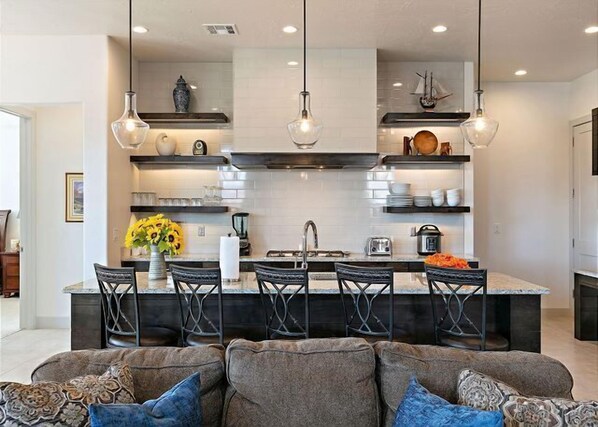 Una cucina moderna con isola centrale, sgabelli da bar, luci a sospensione e un'area pranzo con divano e cuscini decorati.