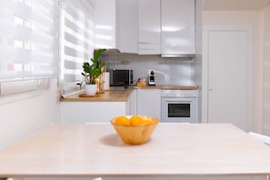 A modern kitchen with white cabinets, a microwave, an oven, and a wooden table with a bowl of oranges. - A calming two-bedroom apartment across from the Prado Museum, on Madrid's most noble avenue, where soft light and quiet rooms sit minutes from the Retiro and Barrio de las Letras. (Madrid)