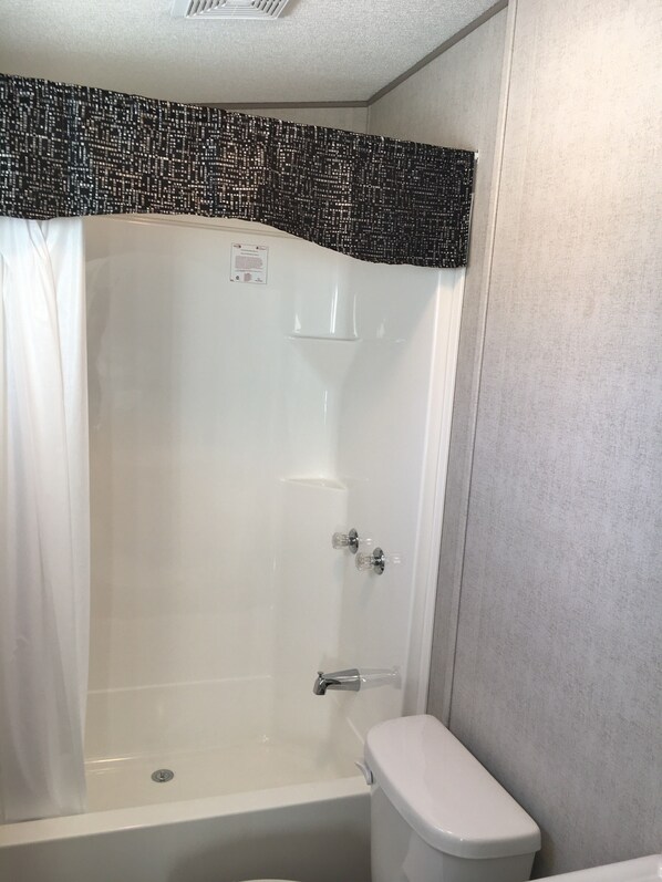 A bathroom with a shower, toilet, and a wall-mounted shelf. - Great Blue Resort Bonnie Lake Resort (Bracebridge)