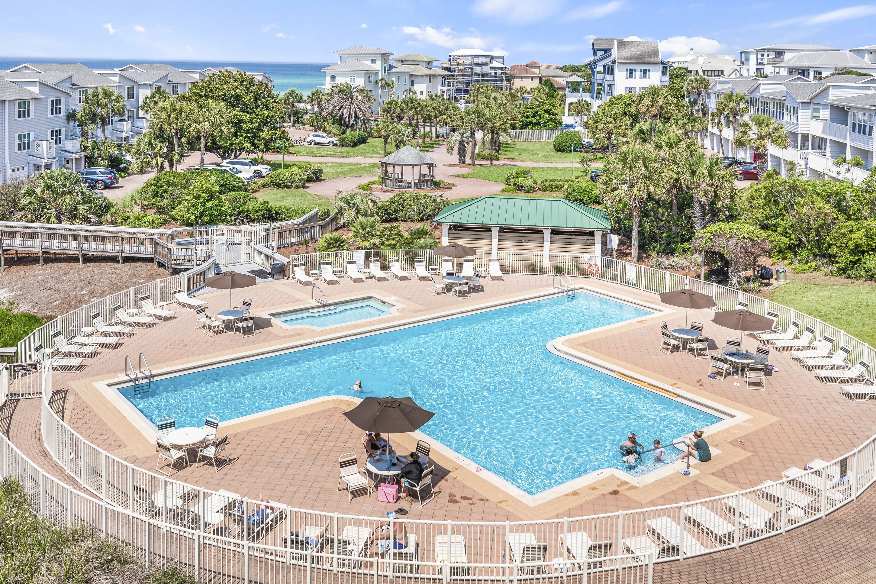 Uma grande piscina ao ar livre rodeada por espreguiçadeiras e guarda-sóis, com vista para o oceano e um complexo de edifícios ao fundo.