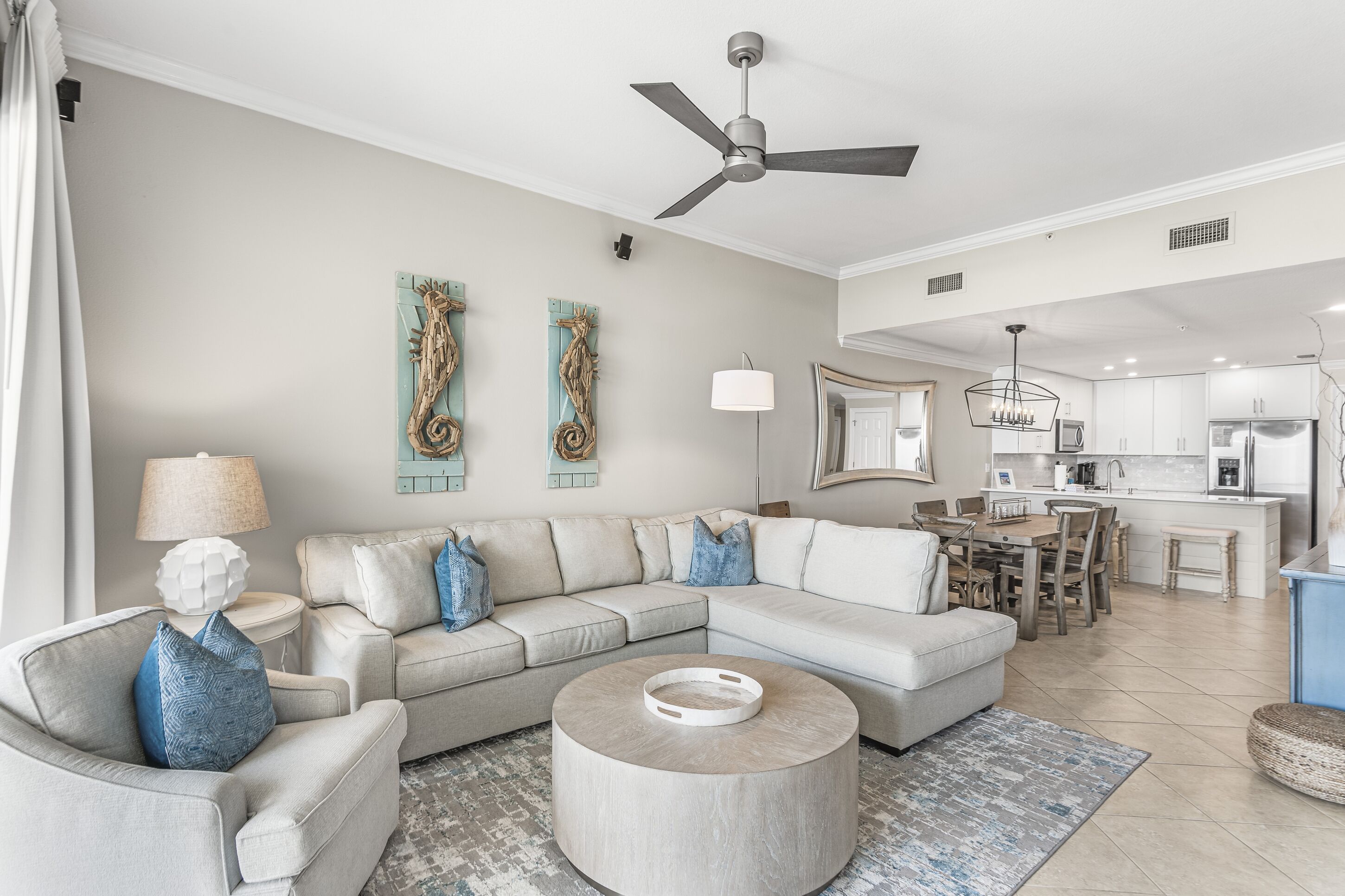 A modern living room with a sectional sofa, a round coffee table, and a dining area with a kitchen in the background.