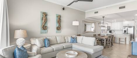 A modern living room with a sectional sofa, a round coffee table, and a dining area with a kitchen in the background.