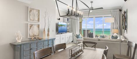 A modern living room with a dining area, a large TV, and a view of the ocean.