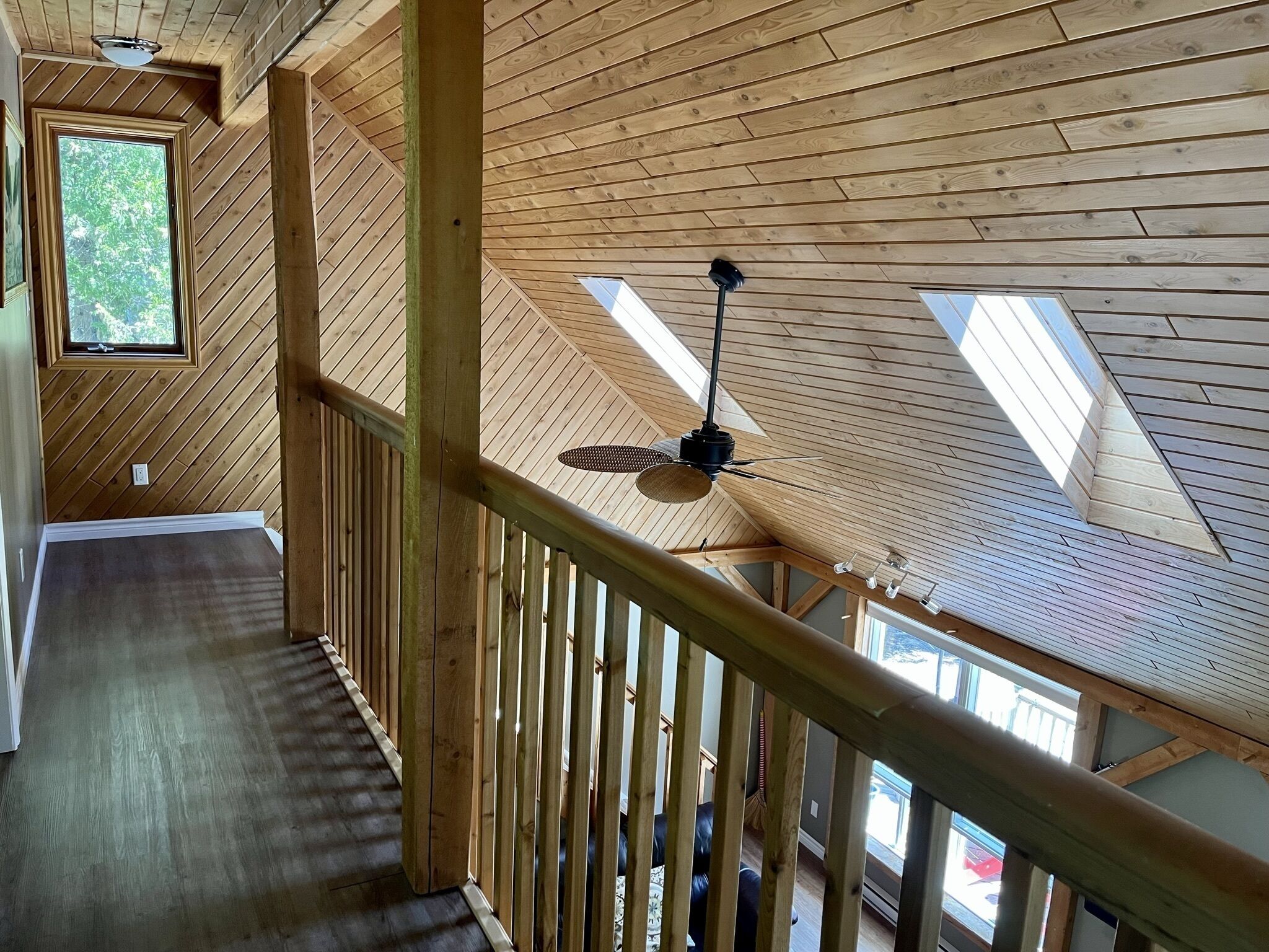 A wooden interior with a sloped ceiling, a ceiling fan, and a view of the outdoors through skylights.
