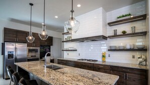 Une cuisine moderne dotée de plans de travail en granit, d’appareils électroménagers en acier inoxydable et de luminaires suspendus.