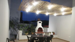 Een terras buiten met een bakoven, verschillende potplanten en een tafel met stoelen.