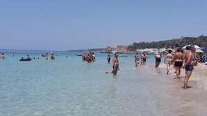 Een strand met helder ondiep water en mensen die zwemmen en over het strand lopen.