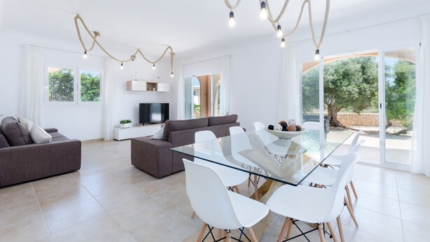 A spacious living room with a glass dining table, two sofas, a flat-screen TV, and a large window offering a view of greenery. - DONES D'AIGUA 11 - Villa with sea views in Urb. S'Estanyol (Colonia de Sant Pere). Free Wi (Artà)