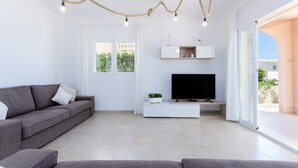 A modern living room with a grey sofa, a flat-screen TV on a white stand, and a large sliding glass door leading to an outdoor area. - DONES D'AIGUA 11 - Villa with sea views in Urb. S'Estanyol (Colonia de Sant Pere). Free Wi (Artà)