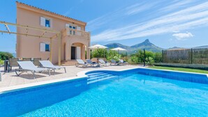 A swimming pool with lounge chairs and umbrellas, a building with a balcony, and a mountainous backdrop. - DONES D'AIGUA 11 - Villa with sea views in Urb. S'Estanyol (Colonia de Sant Pere). Free Wi (Artà)