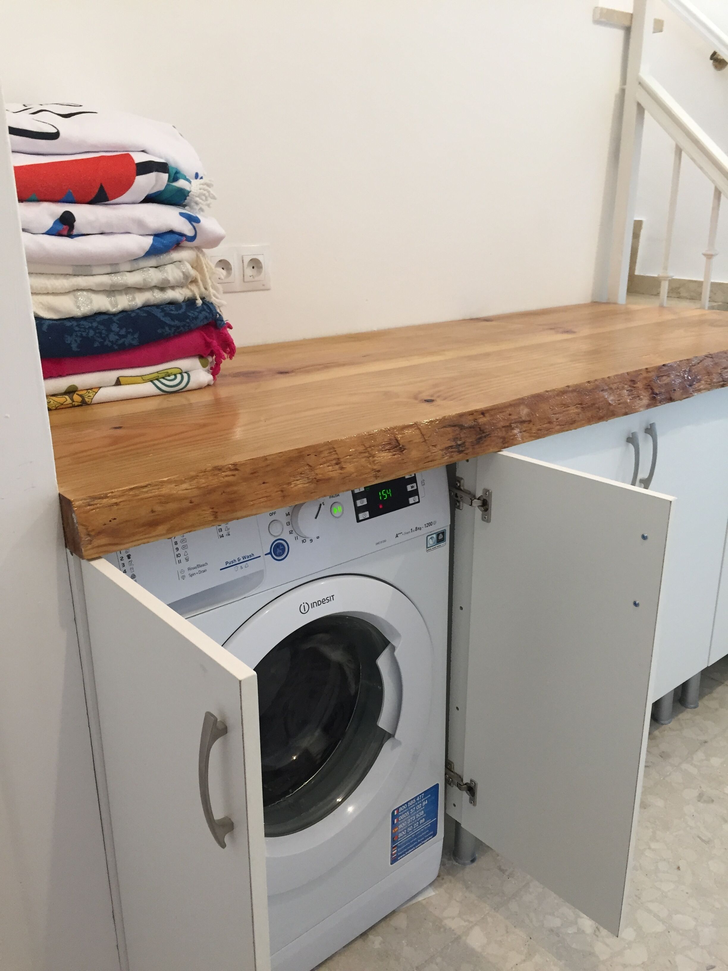Un área de lavandería con lavadora, una encimera de madera y un armario blanco.