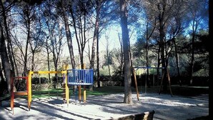 Un parque con un área de juegos, un banco y árboles.