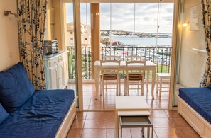 A balcony with a view of the sea and buildings, a dining table with chairs, and blue upholstered seating. - Homerez - Apt near beach & pool (Six-Fours-les-Plages)