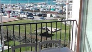 Un balcón con mesa y sillas, con vistas a una marina llena de barcos y una costa lejana.
