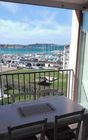 A balcony with a table and chairs, overlooking a marina with boats and a distant coastline. - Homerez - Apt near beach & pool (Six-Fours-les-Plages)