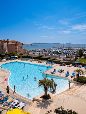 A large swimming pool with multiple lanes, surrounded by sun loungers and a view of a marina with boats. - Homerez - Apt near beach & pool (Six-Fours-les-Plages)
