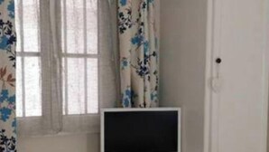 Un dormitorio con cama, televisión sobre un mueble blanco y ventana con cortinas florales.