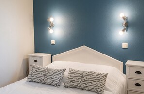 Un dormitori amb un llit blanc, dues taules de nit i llums penjades a la paret.