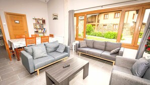 Un salon avec deux canapés gris, une table basse en bois et un coin repas comprenant une table et des chaises.