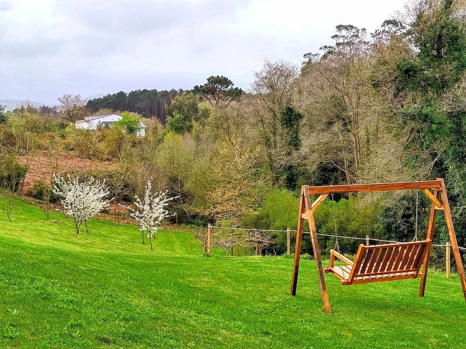 A wooden swing set in a grassy area with trees and a house in the background.