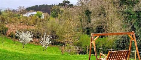 A wooden swing set in a grassy area with trees and a house in the background.