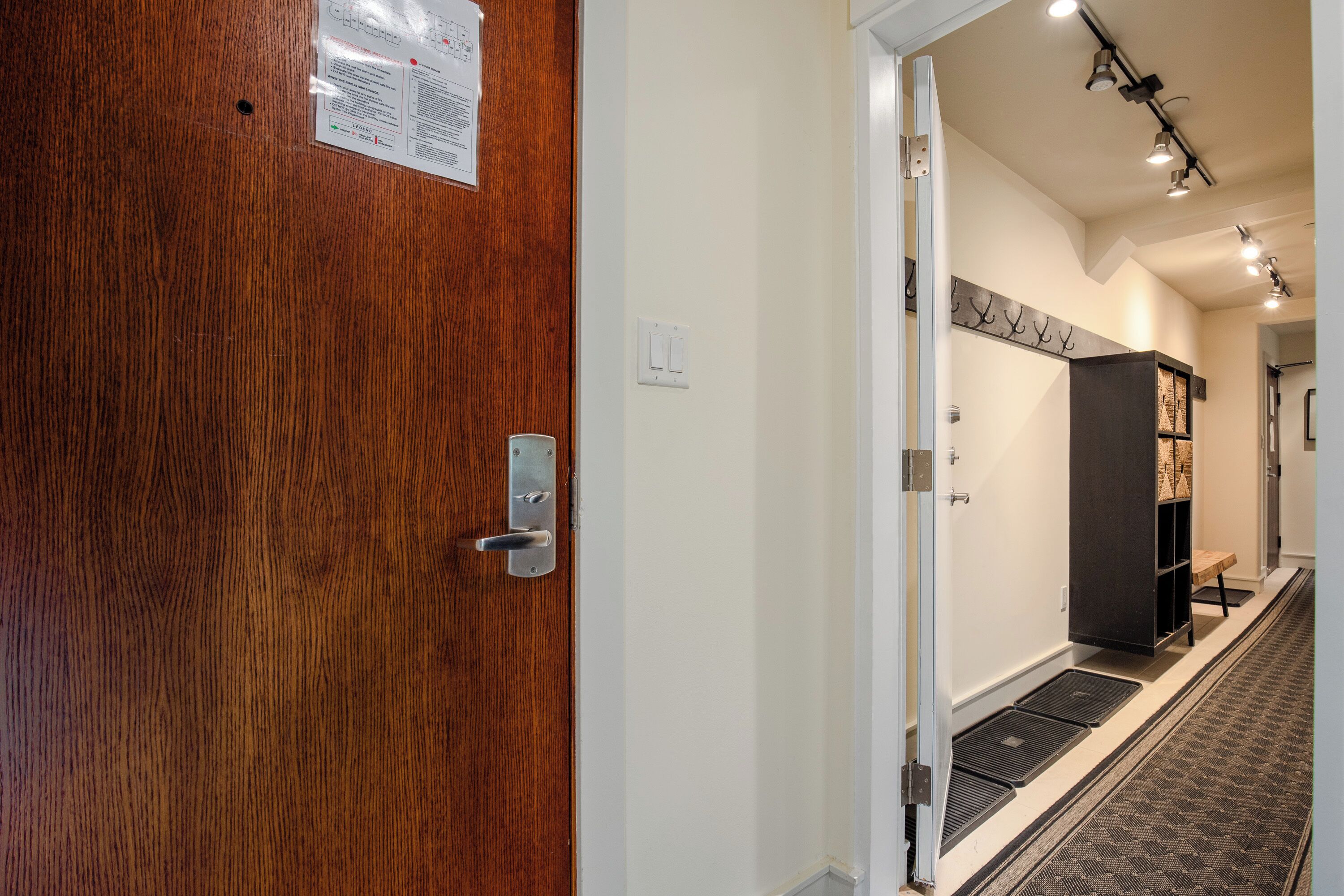 A hotel hallway with a wooden door, a coat rack, and a black cabinet.