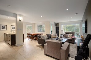 A modern living room with a dining area, kitchen, and large windows.