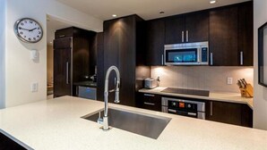 A modern kitchen with dark cabinets, stainless steel appliances, and a built-in sink.
