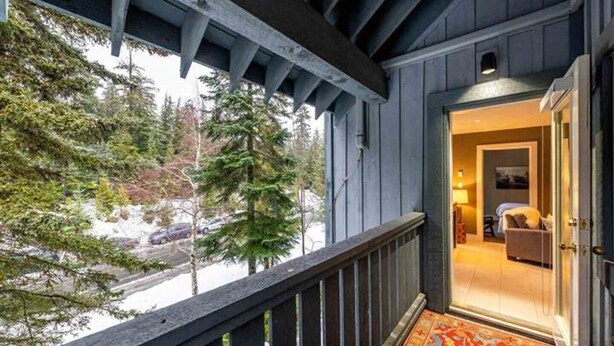 A wooden balcony with a view of trees and a snowy landscape.