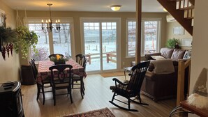 A dining area with a table set for four, a rocking chair, a sofa, and a staircase. - THE HOUSE OF THE RIVER WITH GREAT WATERS #CITQ 299191 (Saint-Laurent-de-l'Île-d'Orléans)