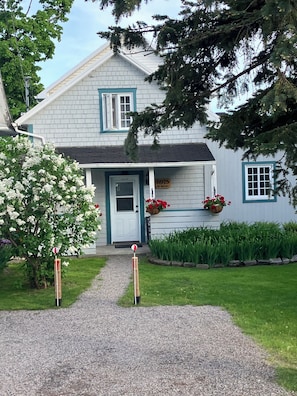 Een huis met een witte gevel, een veranda en een oprit met grind.