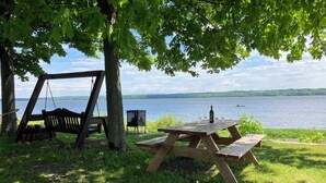 A wooden swing set and picnic table by a lake with a view of the water. - THE HOUSE OF THE RIVER WITH GREAT WATERS #CITQ 299191 (Saint-Laurent-de-l'Île-d'Orléans)