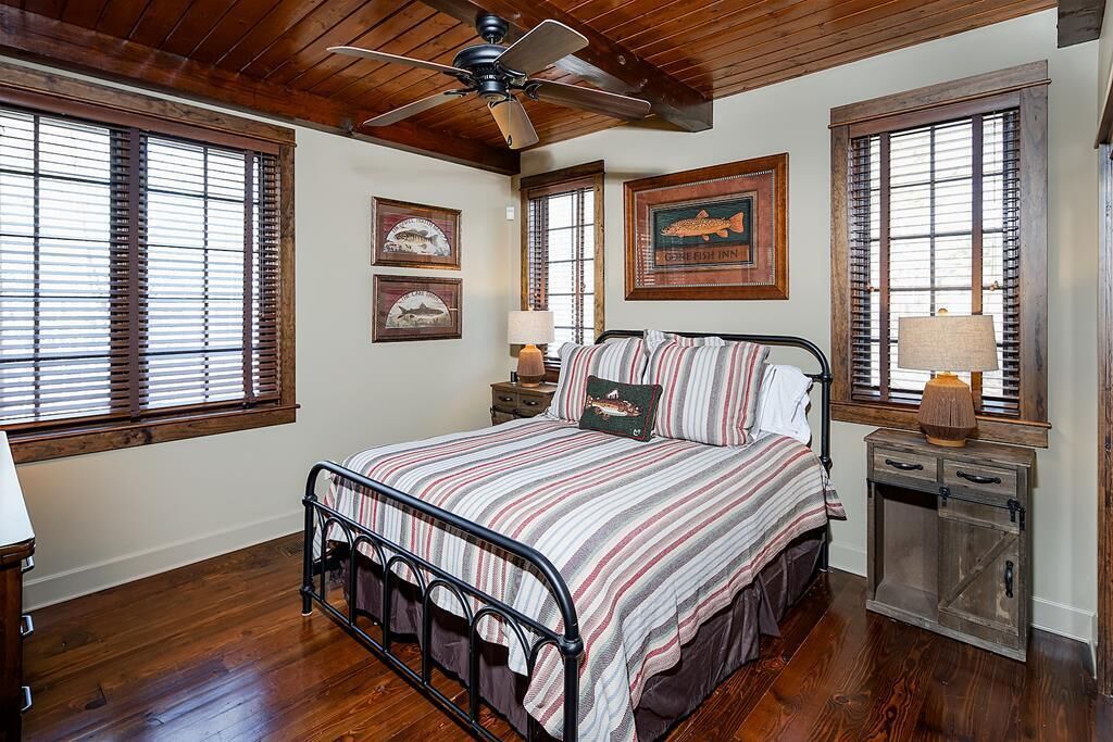 A bedroom with a bed, wooden floors, a ceiling fan, and framed pictures on the wall.