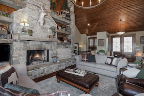A cozy living room with a stone fireplace, a leather ottoman, and a wooden ceiling. - Fontana Lake Lodge: 4BR/4BA lakefront home with hot tub, private dock, game room (Bryson City)