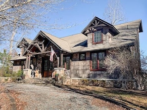 A rustic log cabin with a stone foundation, a prominent American flag, and a large front porch. - Fontana Lake Lodge: 4BR/4BA lakefront home with hot tub, private dock, game room (Bryson City)