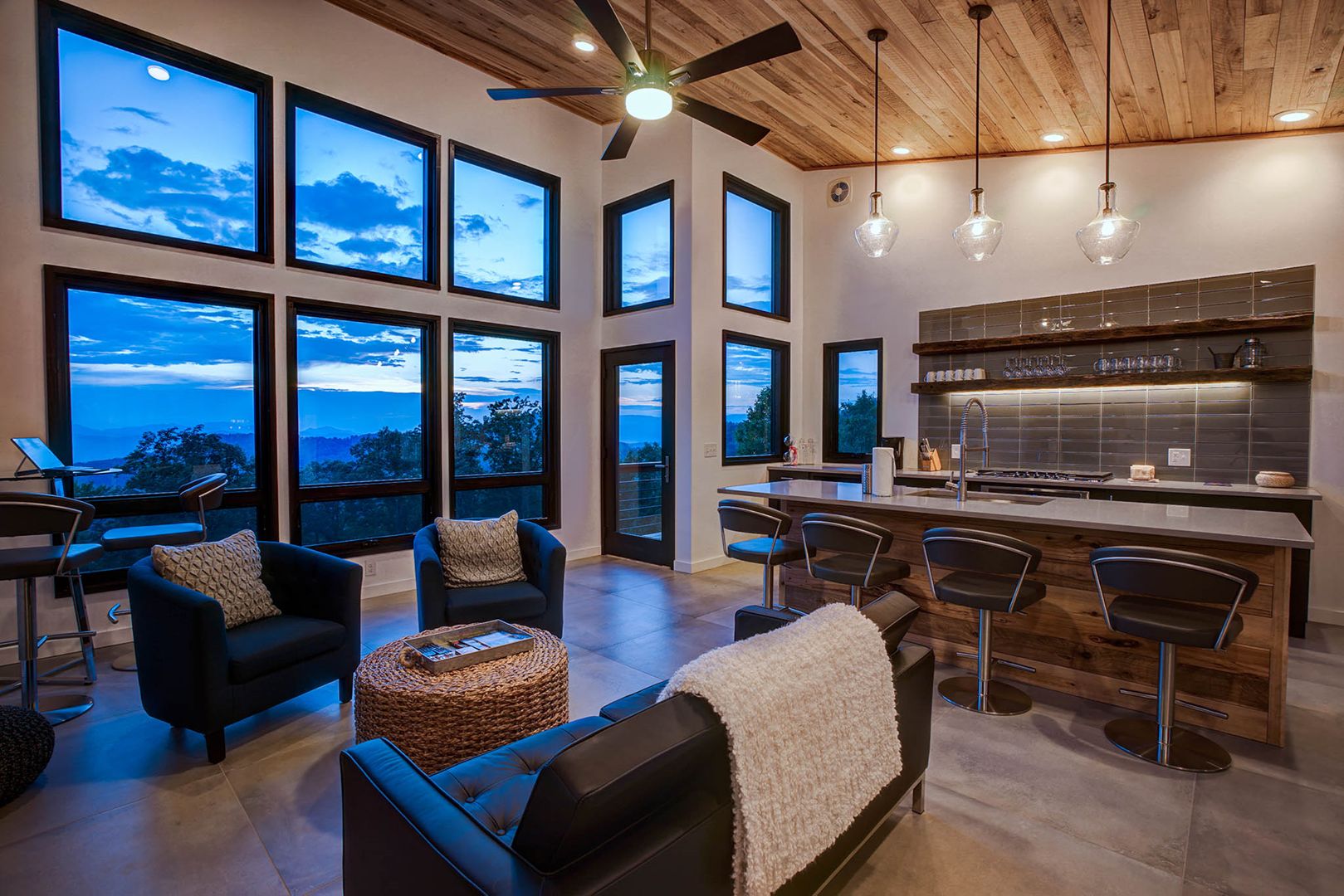 A modern kitchen with a bar area, large windows, and a ceiling fan.