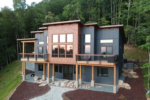 A multi-story modern house with a balcony on the ground floor, surrounded by a forested area. - 3BR mountain-modern cabin with exceptional views, fireplace, and fire pit. Free rafting train passes (Bryson City)