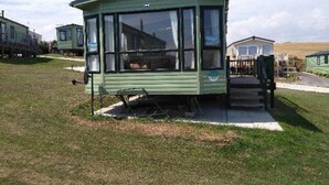 En grøn campingvogn med et stort vindue, en bænk udenfor og en lille veranda.