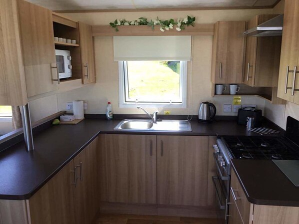 A compact kitchen with wooden cabinets, a sink, a stove, and a window with a view of greenery.