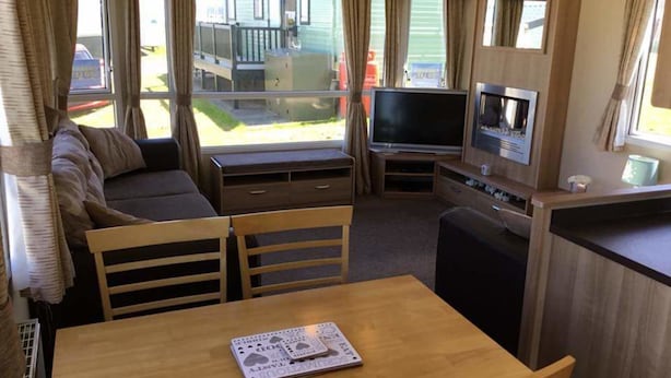 En kompakt autocamper indretning med sofa, spisebord, TV og lille tekøkken.