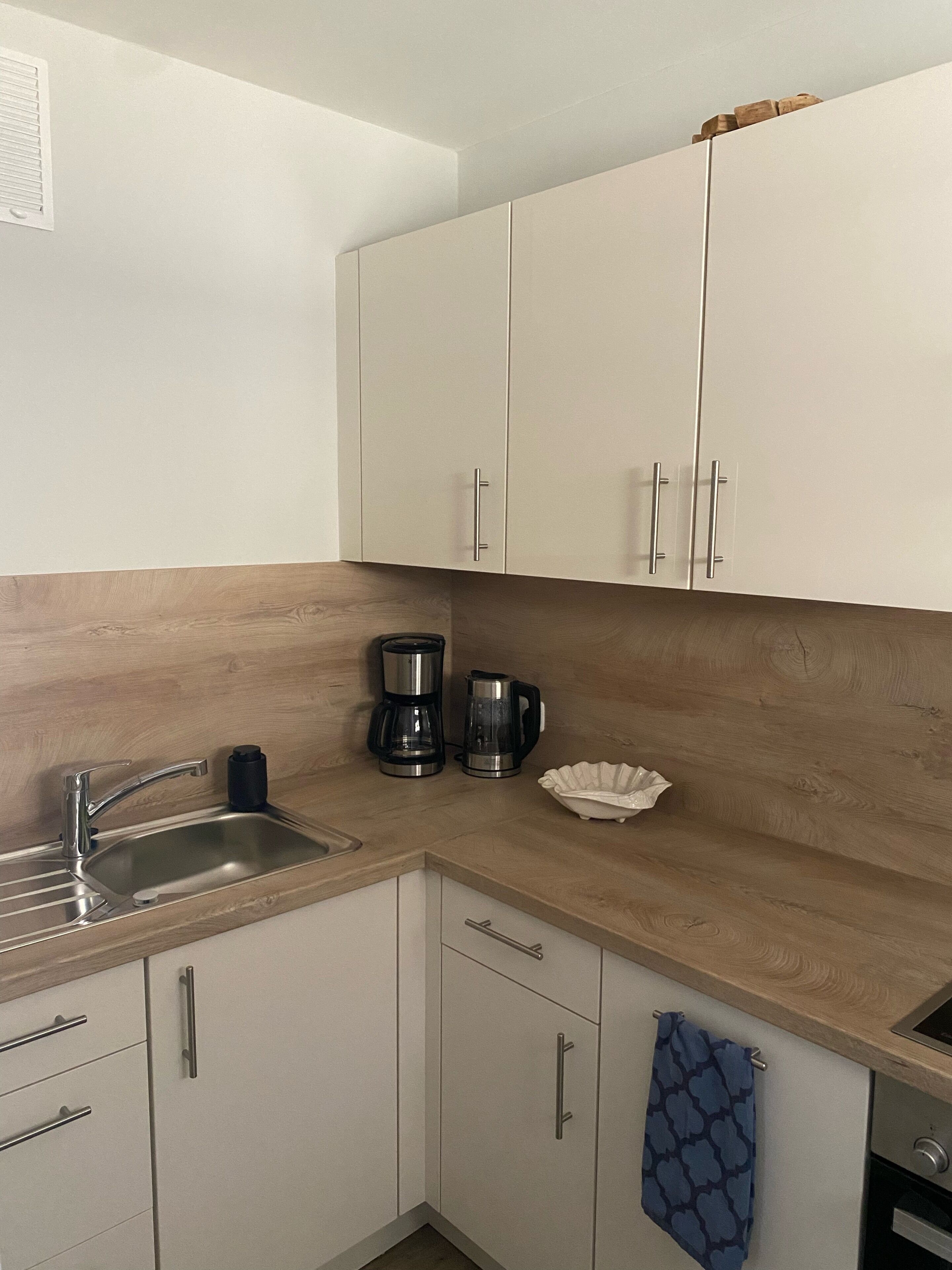 A kitchen with white cabinets, a stainless steel sink, a coffee maker, and a kettle.