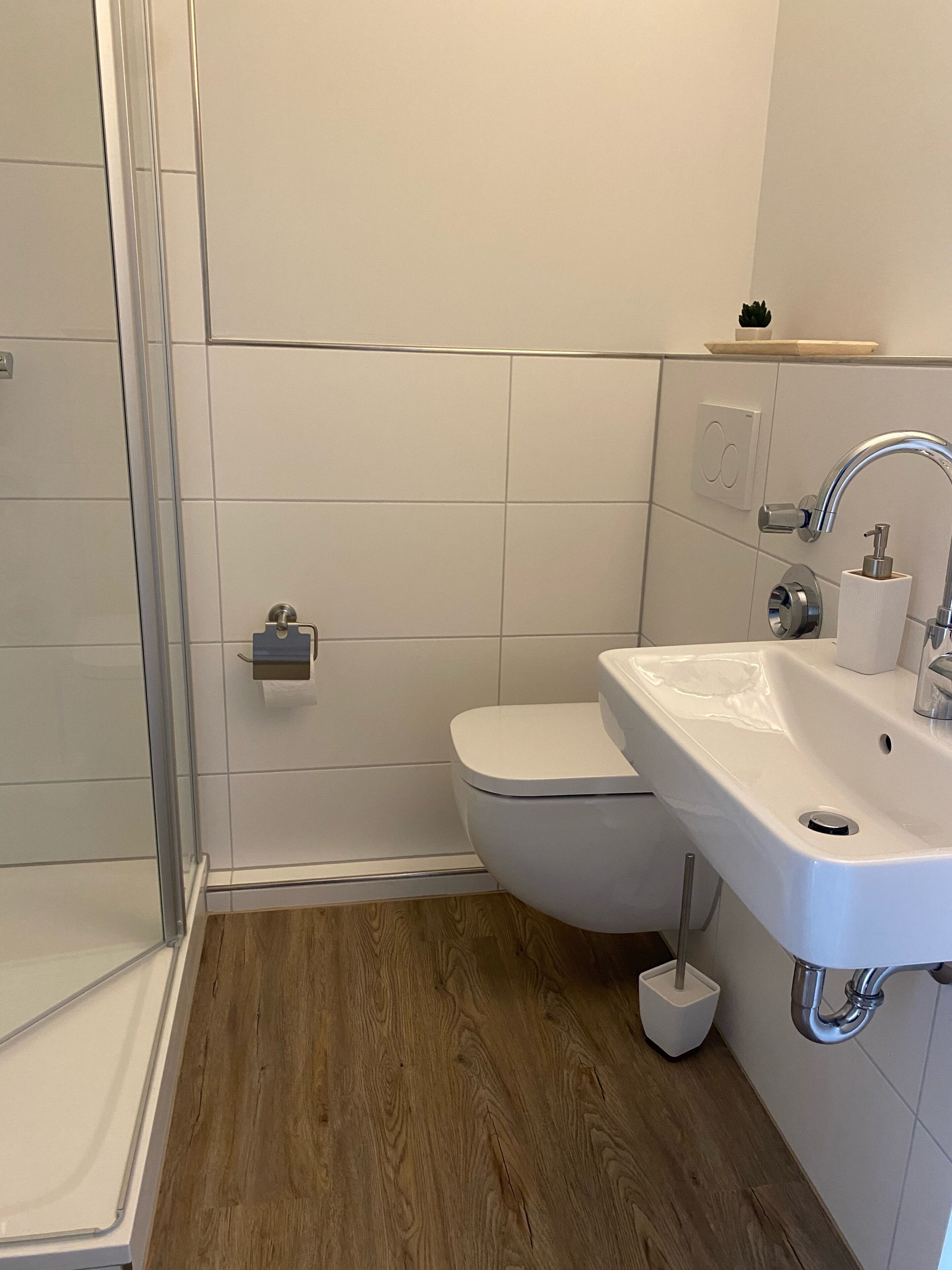 Ein modernes Badezimmer mit Duschabtrennung aus Glas, einer weißen Toilette und einem Waschbecken mit Spiegel.