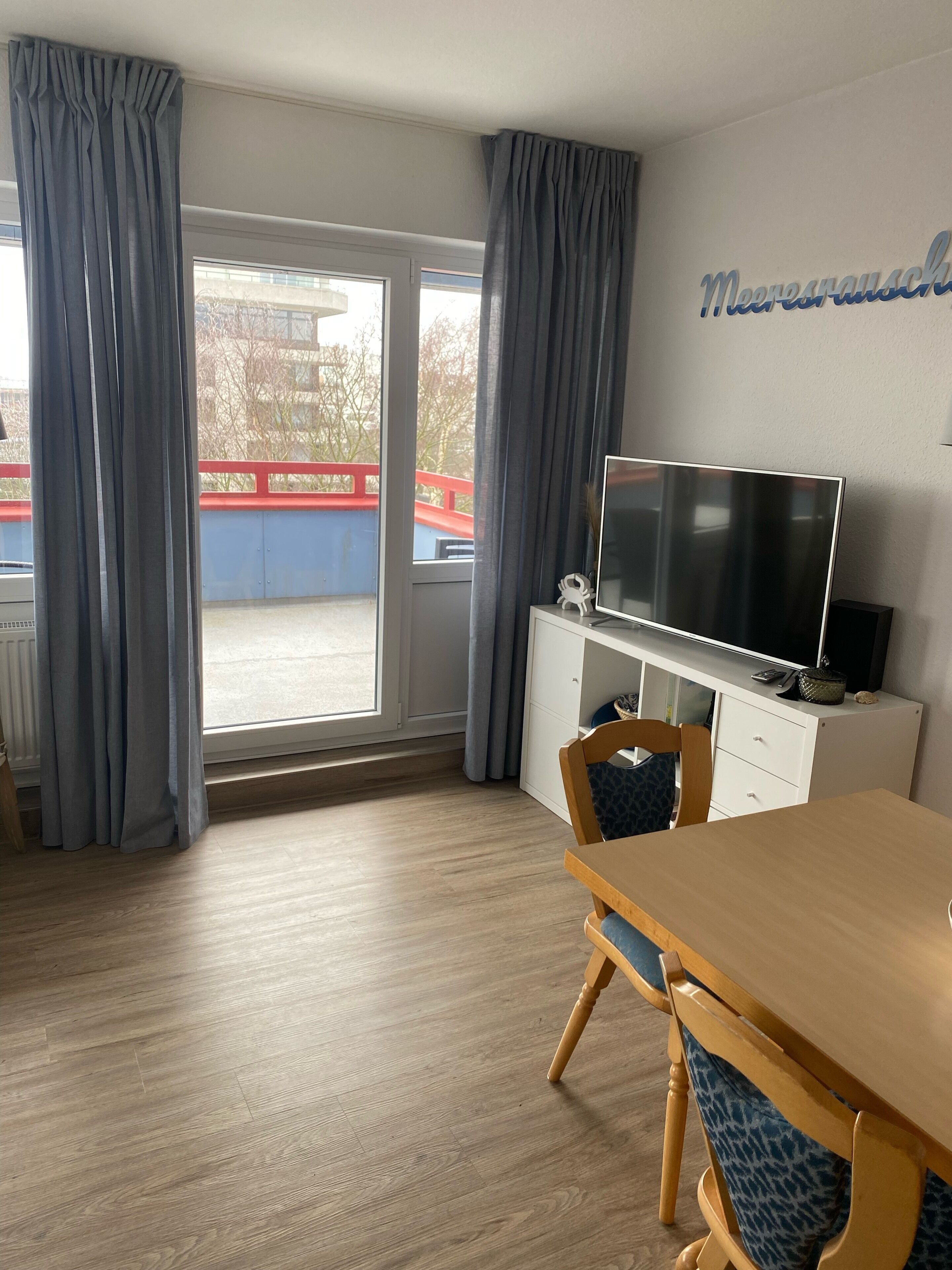 Une chambre d’hôtel avec un plancher en bois, une table à manger avec des chaises, un téléviseur posé sur un meuble blanc, et une vue sur un pont rouge à l’extérieur.