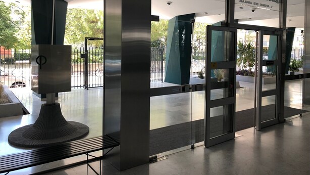 A modern building entrance with glass doors, a metal gate, and a bench outside.